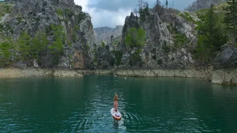 Aerial View: Paddleboarders enjoy emerald waters surrounded by rugged mountains Stock Footage 296190844