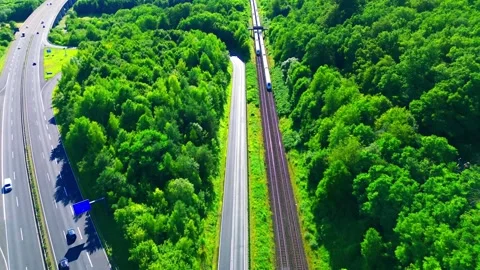 Aerial view of passenger train beside autobahn through green forest in Germany Stock Footage 339415973