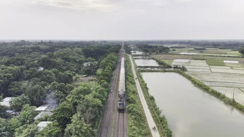 Aerial view of passenger train moving beside green farmland, and ponds Stock Footage 344548065