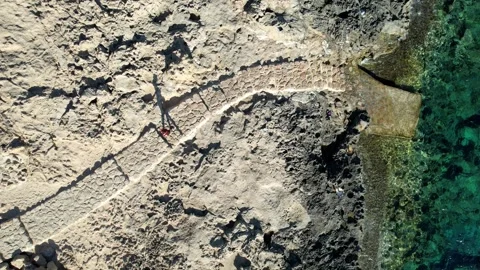 Aerial view of a person walking on a stone path next to the sea Stock Footage 345304489