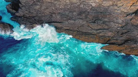 Aerial view of powerful ocean waves crashing against a rugged rocky cliffside Stock Footage 345484115