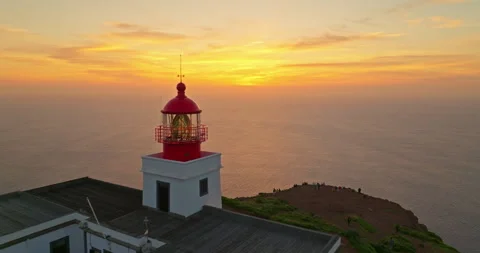Aerial view to red and white lighthouse building on sheer rocky cliff at sunset Stockbeeldmateriaal 271052088