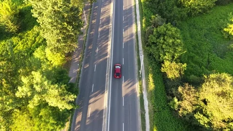 Aerial view of a red car driving along a summer road surrounded by greenery Vídeos de archivo 341472825