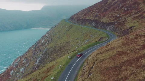 Aerial view of red car moving on beautiful curved costal road Stock Footage
