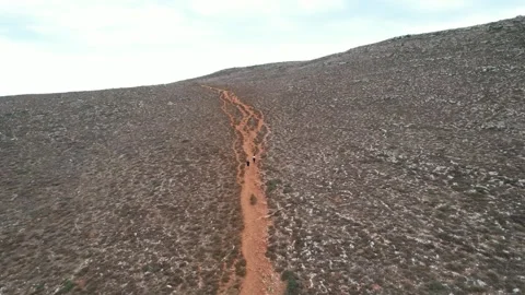 Aerial view of red dirt mountain road crossing barren rocky terrain Greece Stock Footage 344093791