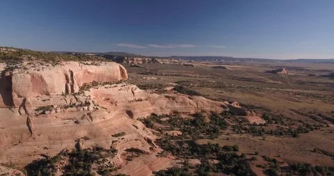 Aerial view of red mountain cliffs and desert landscape with mountains beyond Stock Footage 99518884
