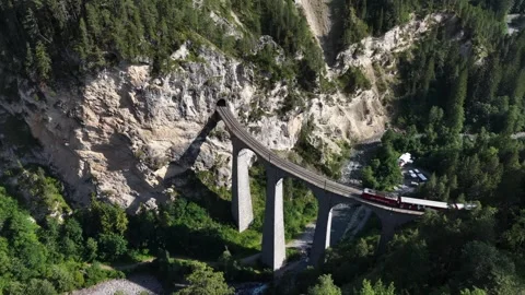 Aerial view of red passenger train crossing landwasser viaduct Stock Footage 318279004