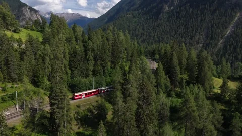 Aerial view of a red passenger train traveling through the swiss alps Stock Footage 318365155