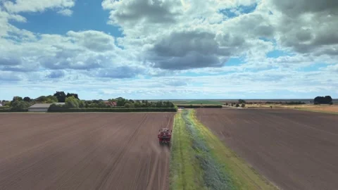 Aerial view of a red tractor plowing vast farmland. Clouds drift above the Stock Footage 345668277