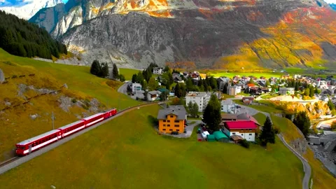 Aerial View of Red Train Passing Swiss Village with Grazing Cows Stock Footage 346731335