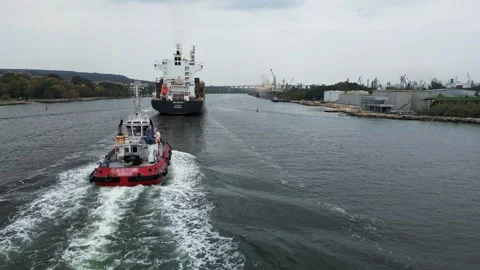 Aerial view of a red tugboat escorting a large cargo ship through the industrial Stock-Footage 319749531