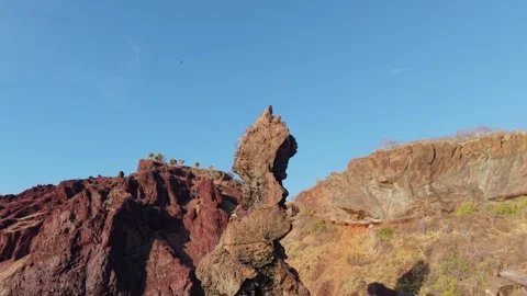Aerial view of red volcanic cliffs towering over blue ocean, rock amid rugged Stock Footage 308420756