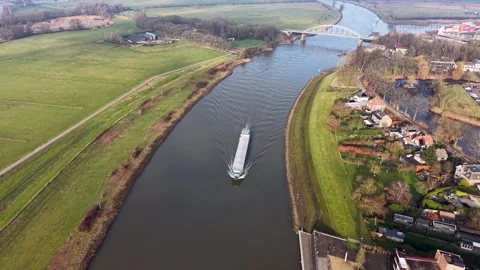 Aerial view of river with cargo ship, arched bridge, and mixed use banks. Vídeos de archivo 327611011