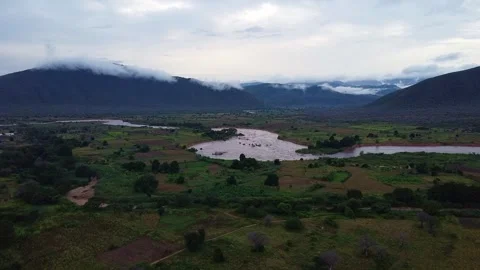 Aerial view of a river flowing through a green valley with mountains and cloudy Stock Footage 313316859