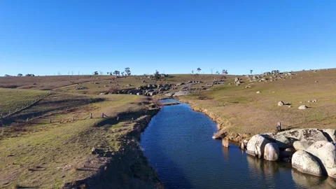 Aerial View of River Flowing Through Grassy Rolling Hills and Boulders Stock Footage 345699846