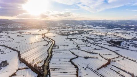 Aerial view of river flowing through snow covered countryside at sunset. Stock Photos
