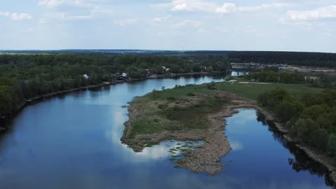 Aerial view of river with reflected blue sky and clouds, green meadows with Stock Footage 107671293