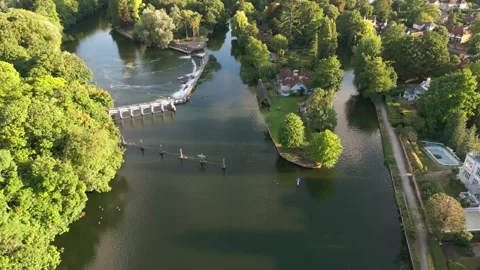 Aerial view of a river with a weir, lush green trees, and houses along the .. Stock Footage 340505749