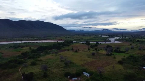 Aerial view of a river winding through a valley with mountains and cloudy sky in Stock Footage 313316616