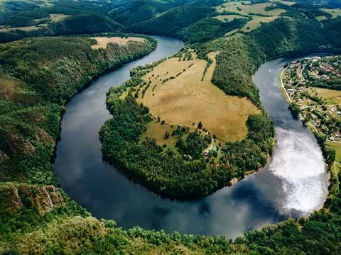 Aerial view of a river winding through lush green hills and forests, with fie Stock Photos