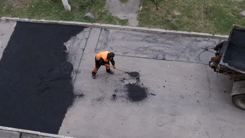 Aerial view of a road construction worker manually spreading asphalt with a.. Stock Footage 339802149