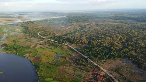 Aerial view of a road cutting through a lush landscape with a lake and dense Stock Footage 316950956