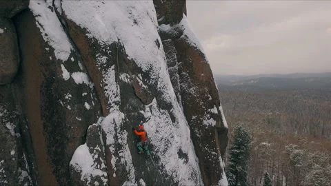 Aerial view of a rock climber climbing a steep cliffs during a sunny winter day. Stock Footage 87620003