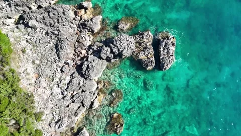 Aerial view of rocky coastline with clear turquoise water, lush green vegetation Stockbeeldmateriaal 337624853