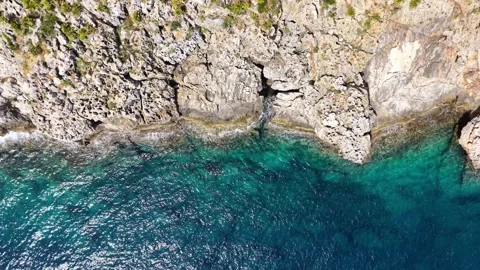 Aerial view of rocky coastline cliffs with sea waves crashing against the shore Stock Footage 345150787