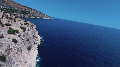 Aerial view of rocky coastline with waves crashing into blue sea Stock Footage 328192544