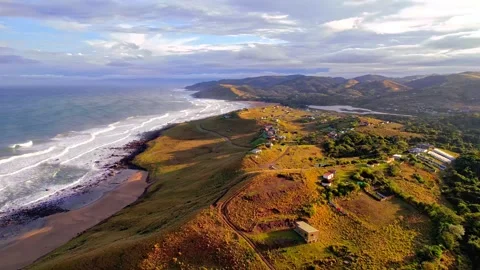 Aerial view of rolling green hills meeting wild ocean waves along pristine Stock Footage 343696505