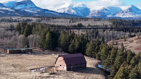 Aerial view of a rustic barn and farmhouse on an open meadow near Whitefish Stock Footage 332379021