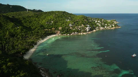 Aerial view of sandy beach with clear bay water in front of green hills on Vidéo 258559576