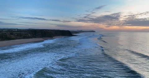 Aerial view of a sandy beach with waves rolling in during the sunset. Drone Stock Footage 221721405