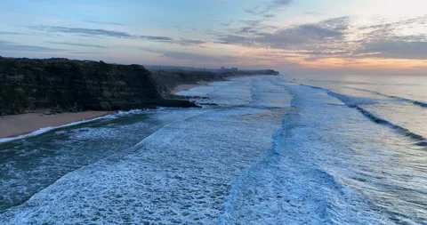 Aerial view of a sandy beach with waves rolling in during the sunset. Drone Stock Footage 222219127