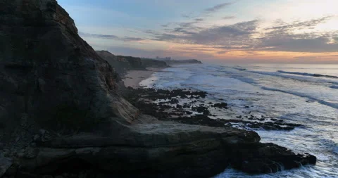 Aerial view of a sandy beach with waves rolling in during the sunset. Drone Stock Footage 222731930