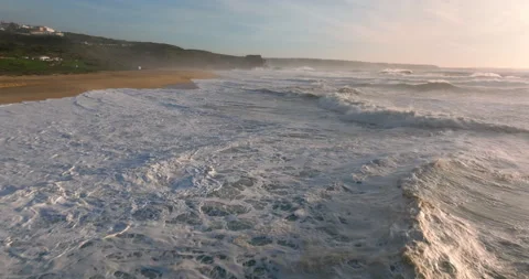 Aerial view of a sandy beach with waves rolling in during the sunset. Drone Stock Footage 224735435