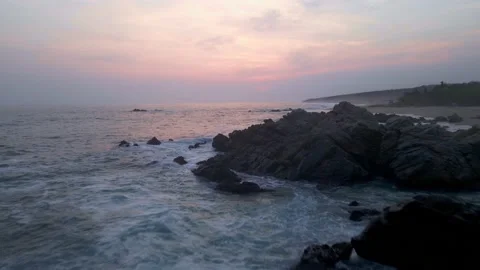 Aerial view of the sea hitting the rocks of the beach shore while the sunset  Stock Footage 155069766