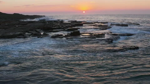Aerial view of the setting sun and waves breaking on the rocks on beach Stock Footage 153759272