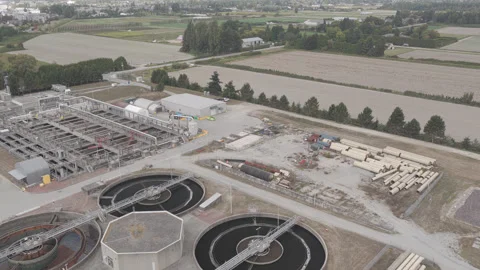 Aerial View of Sewage Clarifier Basins beside Pipe Storage Yard and Farmland Stock Footage 345620265