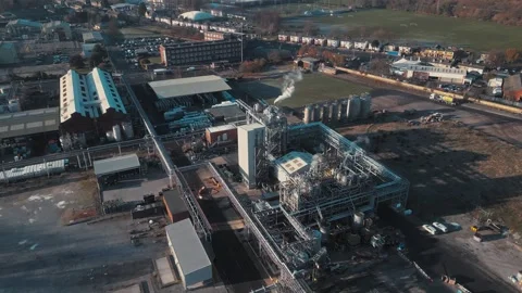 Aerial view shows industrial complex with smoke rising. Buildings, pipes, and Stock Footage 345668804