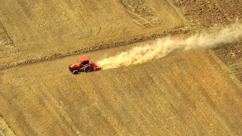 An aerial view shows a red tractor pulling a cultivator across a dry. Stock Footage 274938342