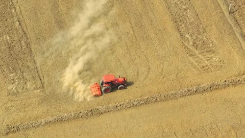 An aerial view shows a red tractor pulling a cultivator across a dry. Stock Footage 274938348