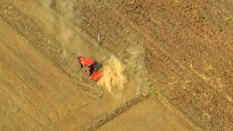 An aerial view shows a red tractor pulling a cultivator across a dry. Stock Footage 274938367