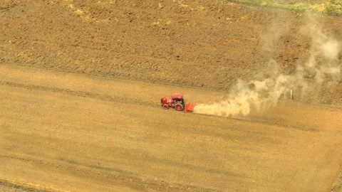 An aerial view shows a red tractor pulling a cultivator across a dry. Stock Footage 274938373