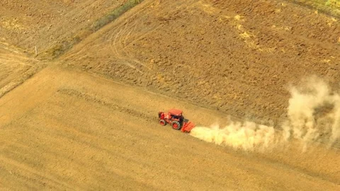 An aerial view shows a red tractor pulling a cultivator across a dry. Stock Footage 274938401