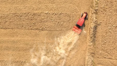 An aerial view shows a red tractor pulling a cultivator across a dry. Stock Footage 274938422