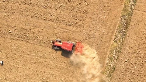 An aerial view shows a red tractor pulling a cultivator across a dry. Stock Footage 274938432