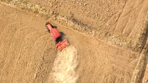 An aerial view shows a red tractor pulling a cultivator across a dry. Stock Footage 274938450