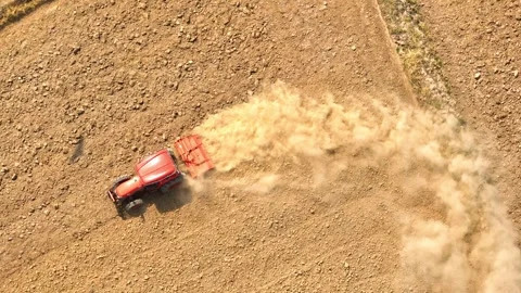 An aerial view shows a red tractor pulling a cultivator across a dry. Stock Footage 274938470
